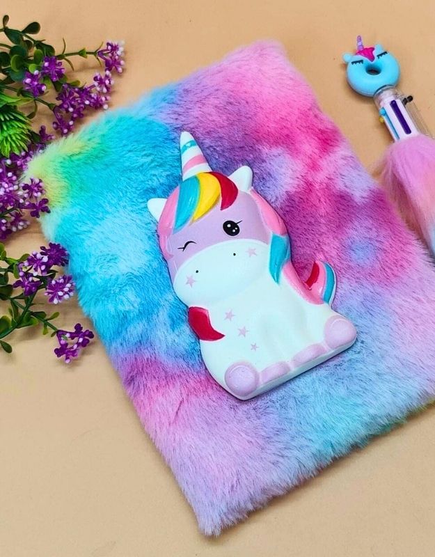 Colorful plush unicorn diary with winking unicorn design and matching pen, surrounded by purple flowers.